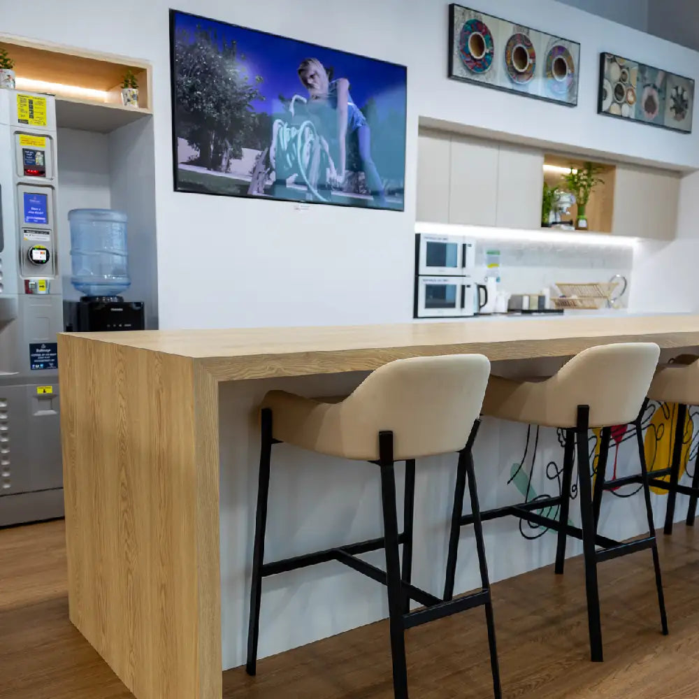 Shared pantry and coffee bar with modern appliances and high stools at Austria Business Center, Al Hudaiba Mall.